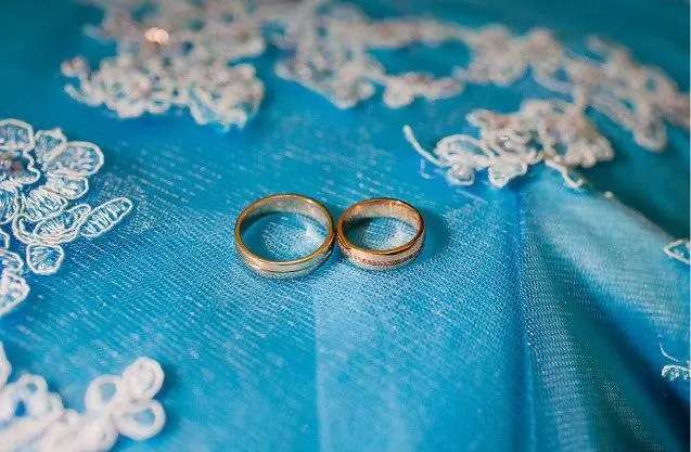Два золоті весільні кільця на бірюзовій тканині з вишивкою.